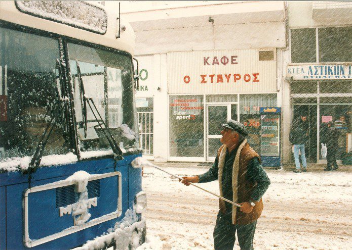A man cleaning the side of a bus on a snowy day.